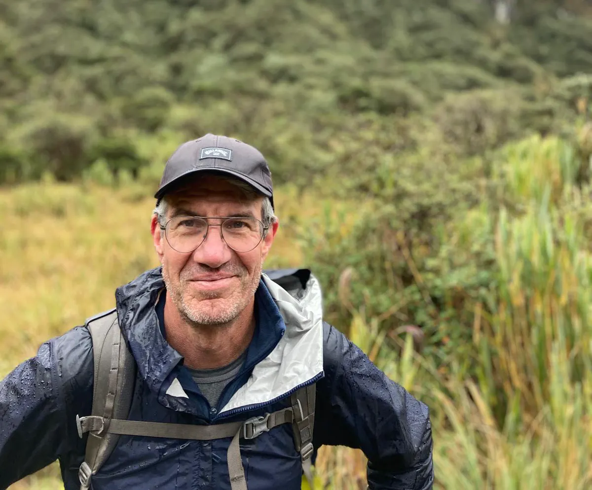Gunthar smiling in rain gear and a backpack, standing in a high-altitude páramo grassland in Ecuador